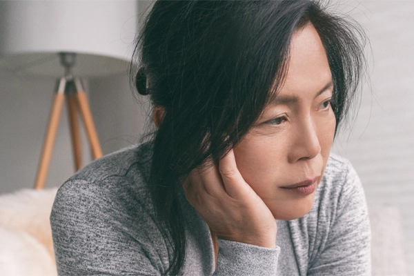 A middle-aged asian woman sitting on her couch, resting her head on her hand, suffering from adrenal fatigue. Get treatment for adrenal fatigue syndrome from Thrive Family Practice & Med Spa in Statesboro.
