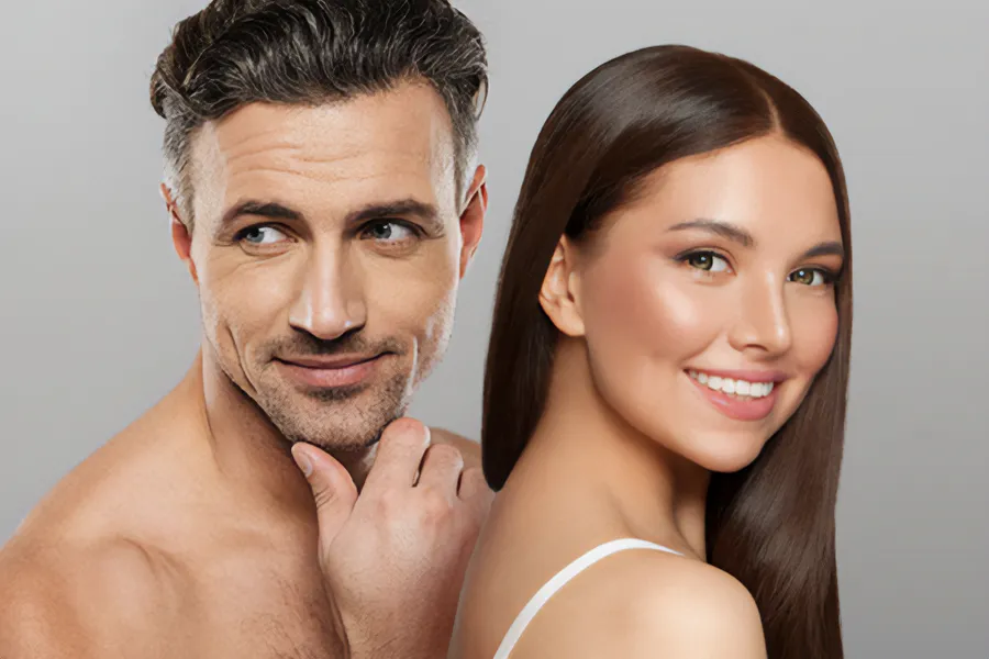 A handsome man and beautiful brunette woman stand against a gray background showing their smooth beautiful skin resulting from aesthetic and cosmetic care from Thrive Family Practice & Med Spa in Statesboro.