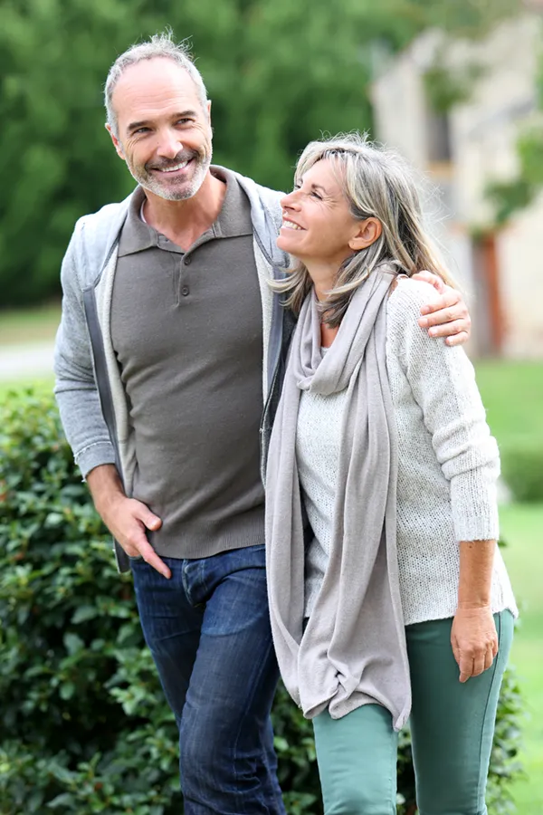 A mature couple in gray toned clothes and jeans walk happily outside, happy with their successful bioidentical hormone treatments from Thrive Family Practice & Med Spa in Statesboro.