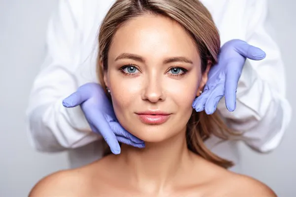 Botox-Doctor Close up of a woman's face with a doctor wearing rubber gloves standing behind her holding his hands around her face to show the amazing Botox Cosmetic treatment from Thrive Family Practice & Med Spa in Statesboro.