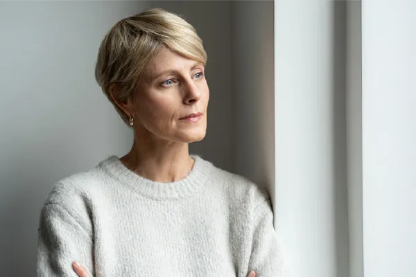 Chronic-Fatigue-Therapy A blond, middle-aged woman looks out the window with a tired expression. Get chronic fatigue treatment from Thrive Family Practice & Med Spa in Statesboro.