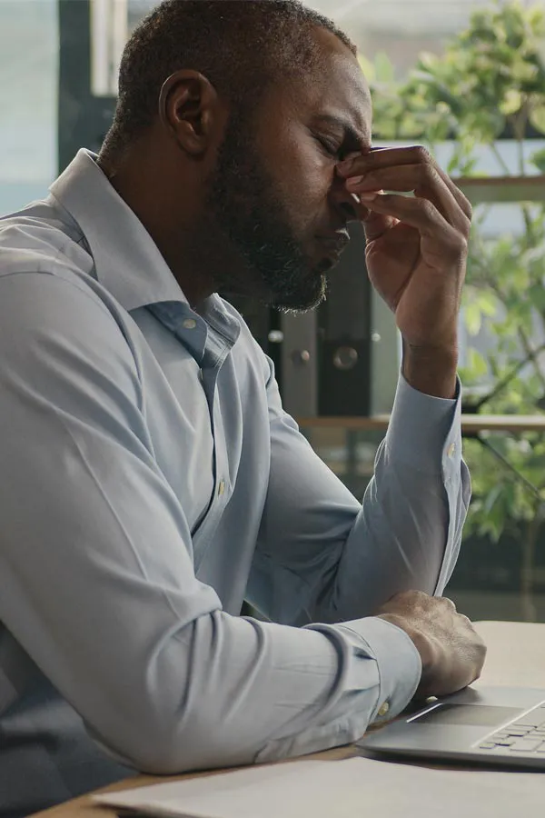 Chronic-Fatigue-Treatment A black man rubbing the top of his nose at his desk, in need of chronic fatigue treatment from Thrive Family Practice & Med Spa in Statesboro.