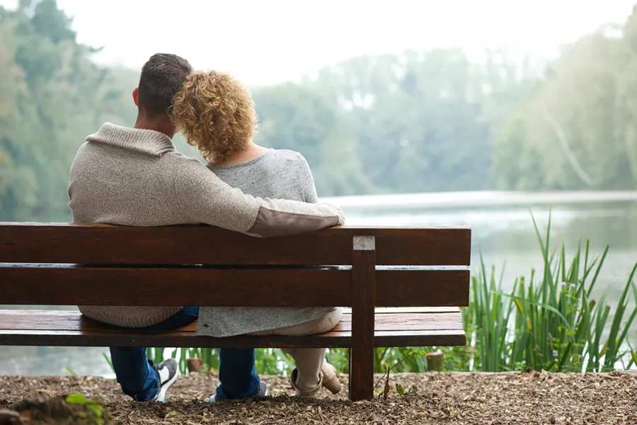 A couple wearing sweaters seen from behind sitting on a bench and looking out at a relaxing lake and forest, representing functional medicine treatment from Thrive Family Practice & Med Spa in Statesboro.