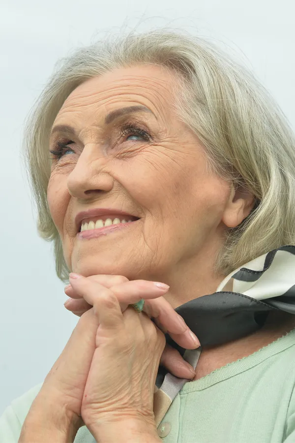 An older woman holds her hands together under her chin and looks up at a cool sky smiling. Get treatment for hot flashes and night sweats from Thrive Family Practice & Med Spa in Statesboro.