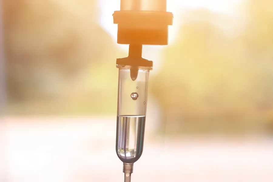 Close-up of an IV drip warmly lit by a window showing trees and a sunset, representing IV therapy from Thrive Family Practice & Med Spa in Statesboro.
