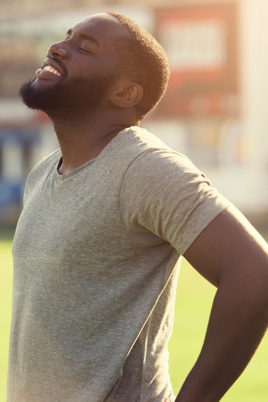 Lean-Muscle-and-Recovery-Treatment A black man in a gray t-shirt and smiles, looking up with closed eyes after a satisfying workout. Get treatment for lean muscle loss and recovery from Thrive Family Practice & Med Spa in Statesboro.