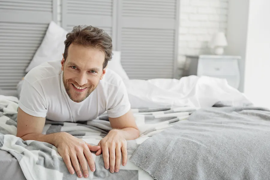 Low-Libido-in-Men-Doctor A dirty-blonde haired man lays on his stomach in bed smiling. Schedule treatment for low libido in men from Thrive Family Practice & Med Spa in Statesboro.