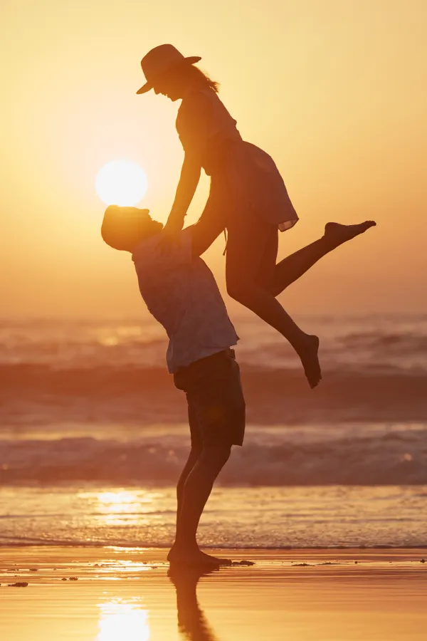 A man lifts up a woman up in joy on the beach at sunset. Get massage therapy from Thrive Family Practice & Med Spa in Statesboro.