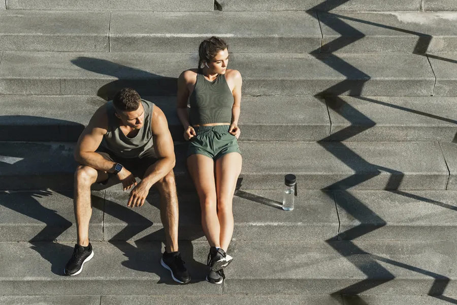 Medical-Weight-Loss-Doctor A couple in gray and green track clothes resting after a workout on stone steps, happy with their weight loss plans from Thrive Family Practice & Med Spa in Statesboro.