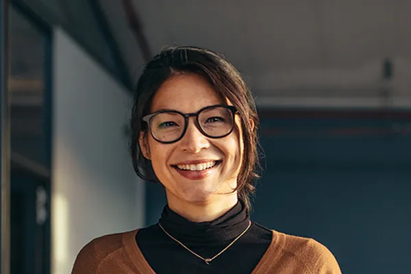A brunette woman with glasses smiles in a gray-blue walled office. Get metabolic syndrome from Thrive Family Practice & Med Spa in Statesboro.