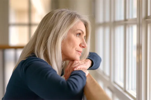 PMDD-Specialist A middle-aged woman with with a somber expression stares out the window. Get treatment for Premenstrual Dysphoric Disorder from Thrive Family Practice & Med Spa in Statesboro.