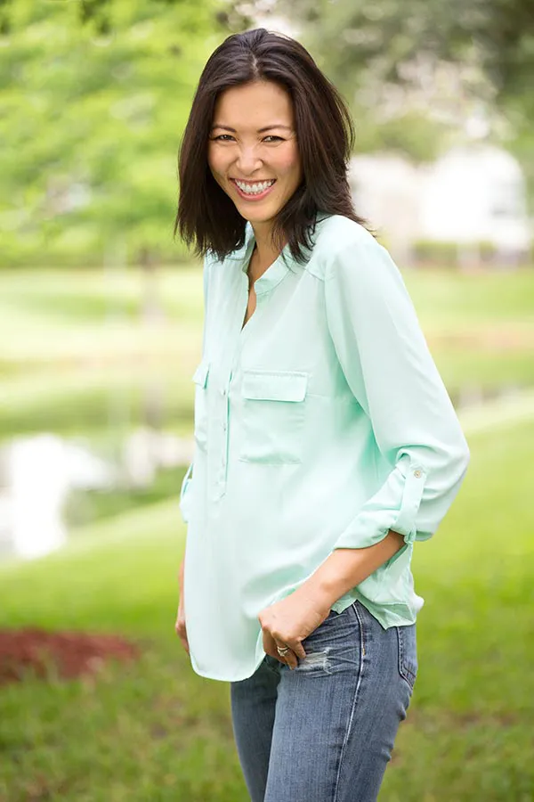 Perimenopause-Treatment A middle-aged brunette woman in a light green button-up shirt stands outside smiling, happy with her perimenopause treatment from Thrive Family Practice & Med Spa in Statesboro.