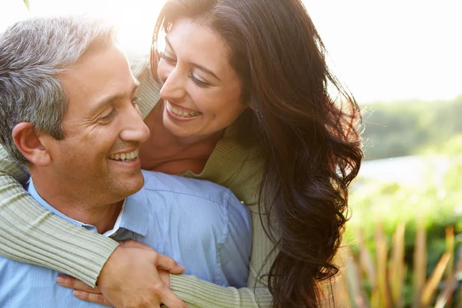 A middle-aged Latin couple embrace each other in a field under the sun. Get Primary Care services from Thrive Family Practice & Med Spa in Statesboro.