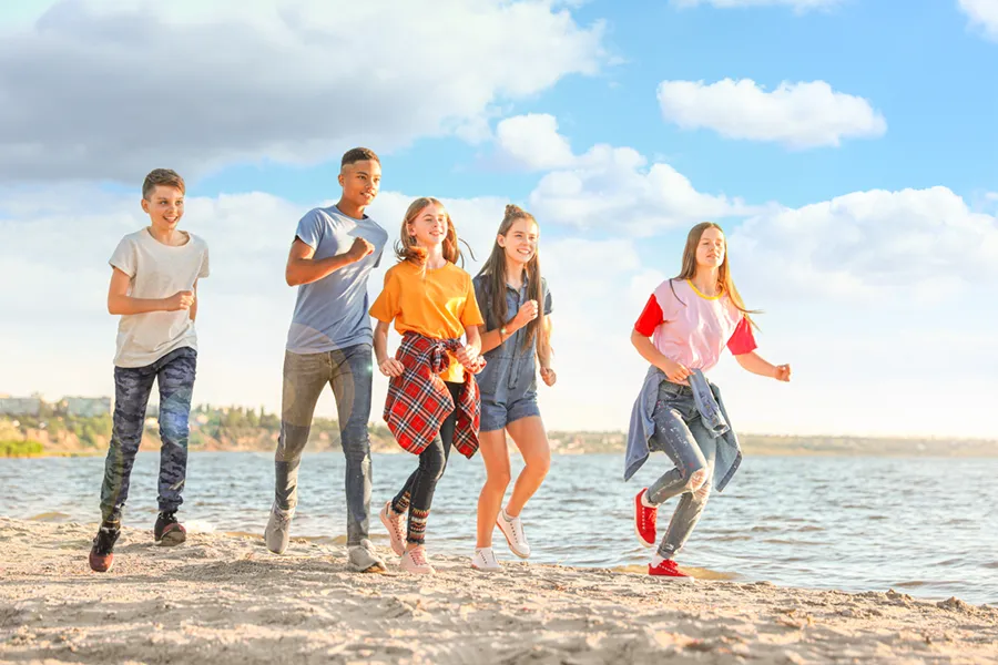 A group of children of various ages, genders and races running on the beach. Schedule sports physicals for children from Thrive Family Practice & Med Spa in Statesboro.