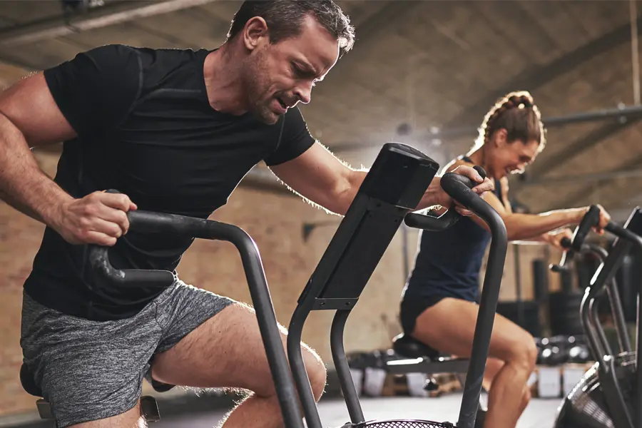 Tirzepatide-Doctor A couple in a brick gym work as hard as they can on exercise bikes, inspired by successful Tirzepatide treatment from Thrive Family Practice & Med Spa in Statesboro.