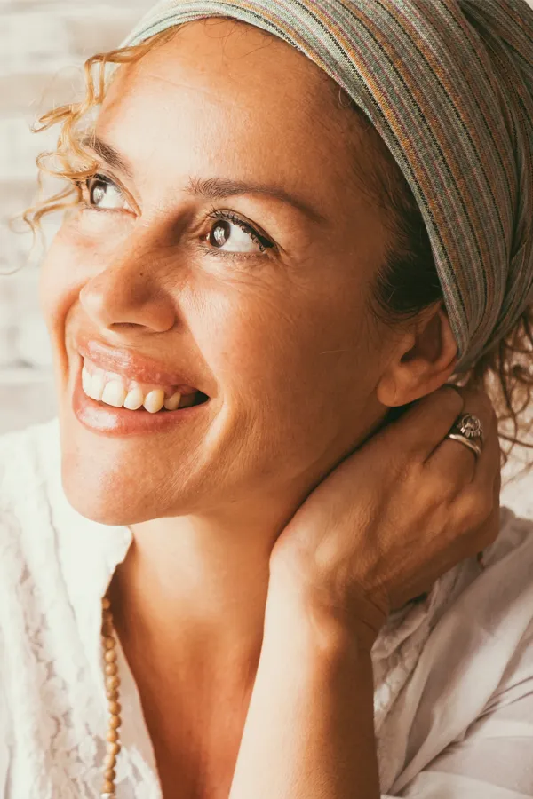 A mixed-race woman looking up to the side and smiling. Get comprehensive women's health exams from Thrive Family Practice & Med Spa in Statesboro.